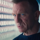 Daniel Craig's James Bond looks at a wall full of colored vials.